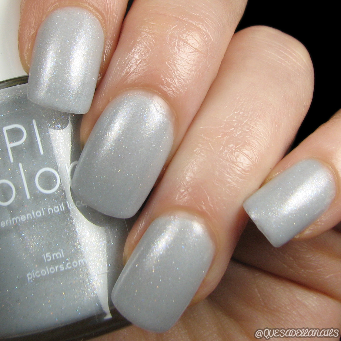 A close-up displays a hand with nails adorned in the luxurious, shimmery hue of silver-grey. The "Storm Morning.062" nail polish bottle from PI Colors is partially visible, showcasing 15ml of handcrafted allure. The neatly manicured nails exude a glossy finish accented by delicate holographic glitter.