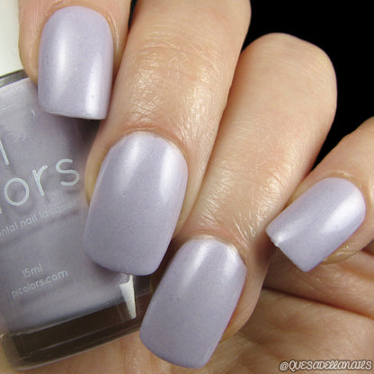 Close-up of a hand with nails painted in PI Colors' Stormshine.029, a satin creme lilac purple shade, holding a matching luxury nail lacquer bottle. The finish has a subtle shimmer. ©quesadewnaies is visible in the bottom right corner.