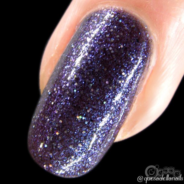 A close-up of a fingernail showcases the dark purple, glittery enchantment of Unicorn Sauce.001 by PI Colors. This handmade nail polish shimmers with tiny specks of light against a black background, adding a touch of magic to its allure.