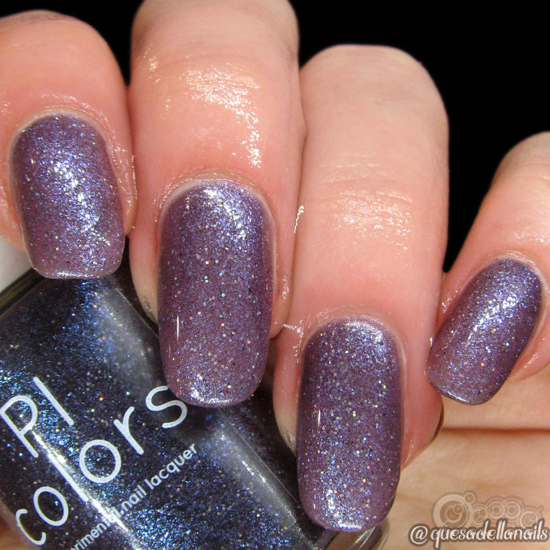 Close-up of a hand with manicured nails painted in glittery purple nail polish. The thumb holds a bottle of PI Colors' Unicorn Sauce.001, perfectly matching the nails. The glitter shimmers like black blue glitter as the thermal color-changing polish reveals deeper hues in varying temperatures. Nails are evenly shaped and well-polished.