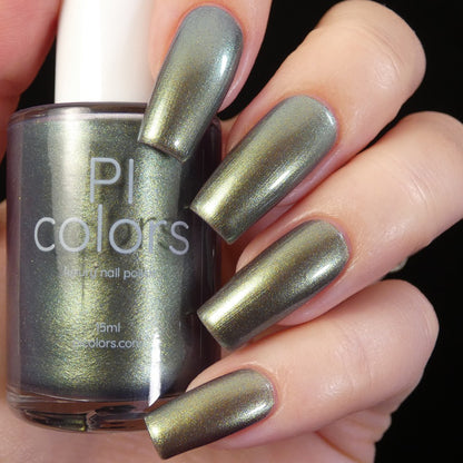 A hand with long fingernails painted in shimmering multi-chrome green holds a bottle of "Light/Forest.000 Green Nail Polish" from PI Colors, showcasing its opulent, handmade brilliance.