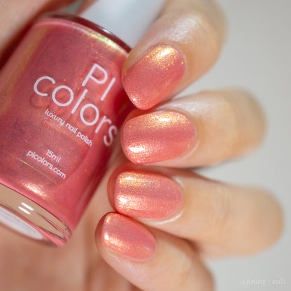 A close-up shot captures a hand with nails adorned in a shimmery coral pink polish from PI Colors, showcasing their Alstroemeria.000 Luxury Nail Lacquer. The bottle displays the same radiant shade, complete with a luxurious finish and subtle gold flecks.