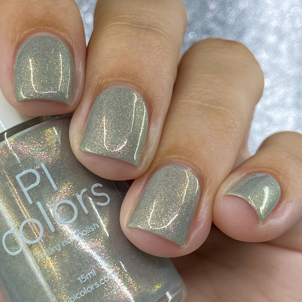 Close-up of fingers adorned with shiny gray nail polish, featuring a bottle labeled "PI Colors." The nails exhibit a subtle holographic sheen, evocative of the ToW.001 Taupe Nail Polish's shimmering aurora lacquer.