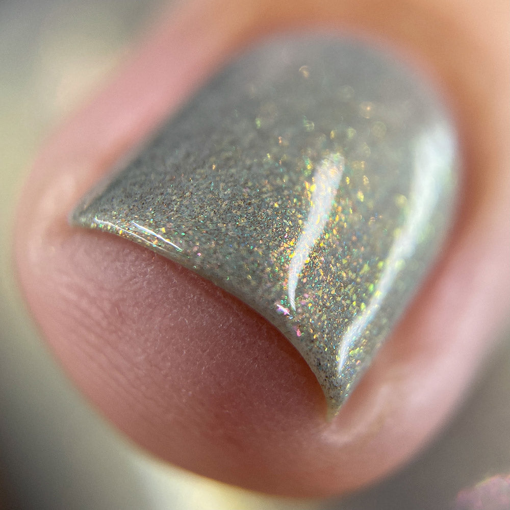 A close-up of a fingernail adorned with ToW.001 Taupe Nail Polish by PI Colors reveals shimmering aurora lacquer and iridescent sparkles reflecting light. This 10-free nail polish highlights a well-groomed nail at the center, showcasing its smooth and glossy texture vividly.