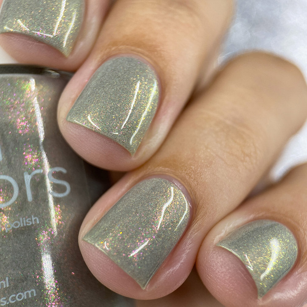 Close-up of a hand showcasing nails adorned with the shimmering aurora lacquer known as "ToW.001 Taupe" from PI Colors, featuring a shimmery gray tone. The 10-free polish bottle is partially visible, catching the light and highlighting its subtle glitter particles.
