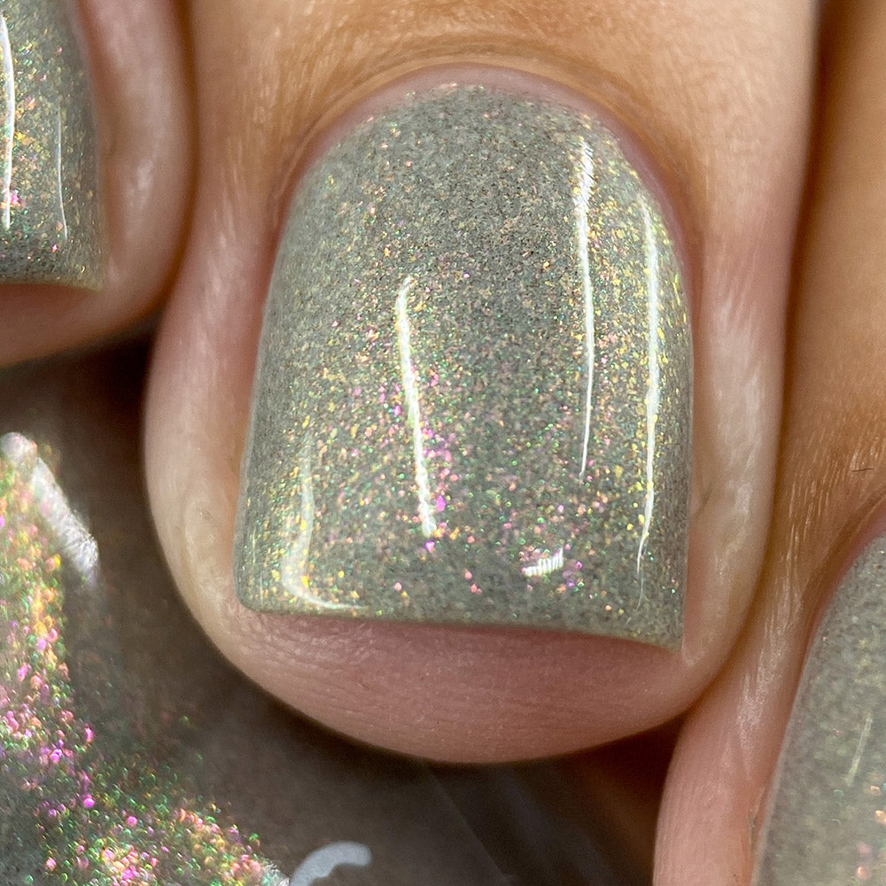 Close-up of nails adorned with PI Colors' ToW.001 Taupe Nail Polish, a light gray-green hue featuring dazzling pink and gold shimmers that create a glittery effect when illuminated. This nail lacquer is formulated without 10 common toxins for a healthier manicure experience.