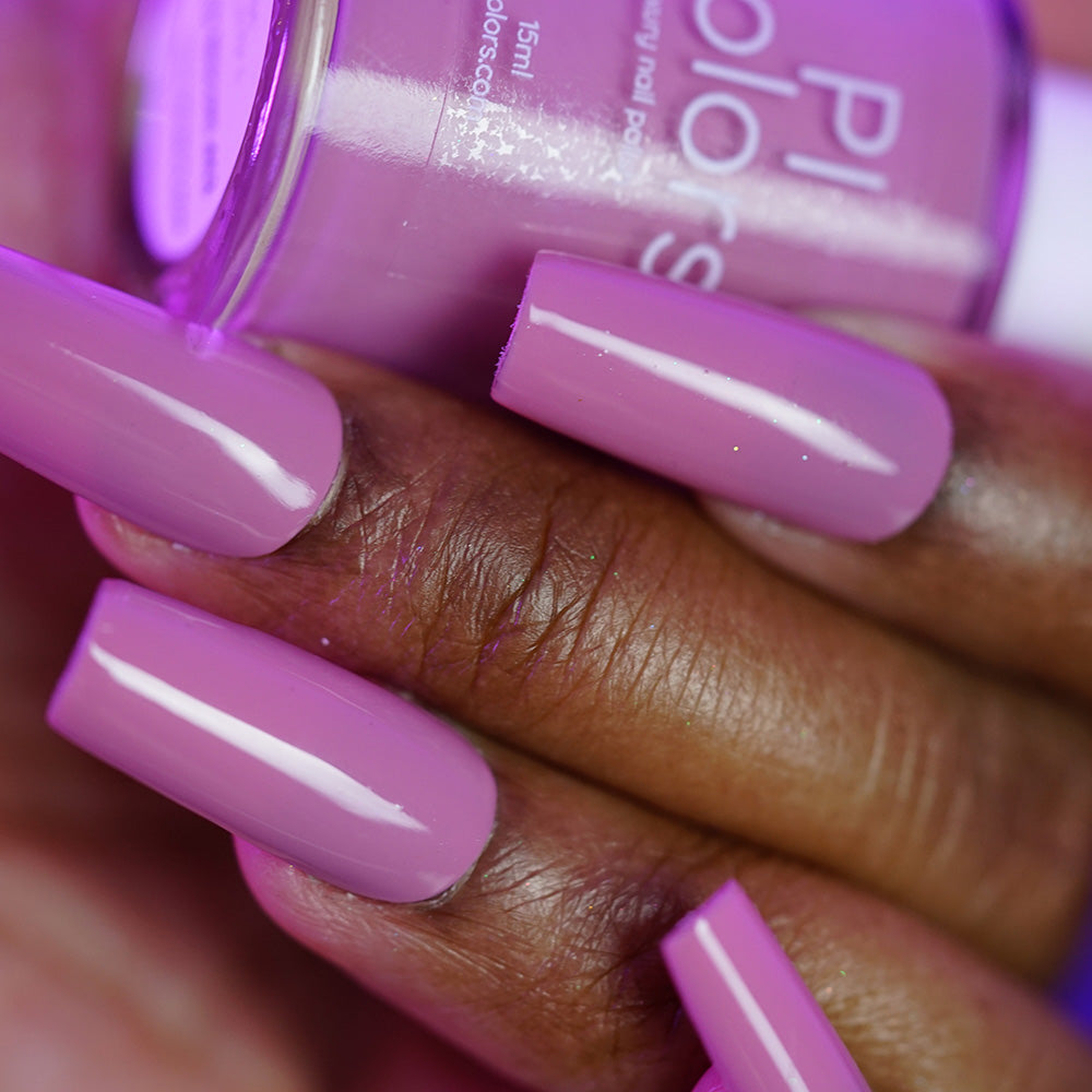 A close-up of a hand with dark skin wearing PI Colors Pink Biscotti.462, a long, glossy brownish pink creme handmade nail polish, holding the matching bottle.