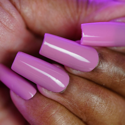 A close-up of a hand with long, square acrylic nails painted in PI Colors’ Pink Biscotti.462, a glossy brownish-pink creme polish. The slightly curled fingers highlight the shiny finish.