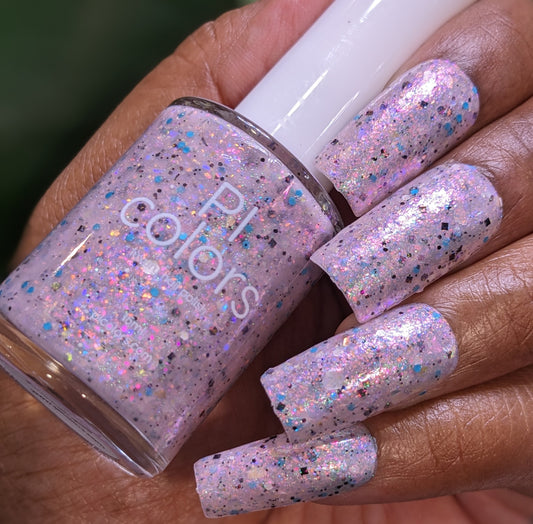 A hand with long fingernails showcases sparkly pink polish with luxury iridescent blue and silver flakies. A matching "Pink Ash.305" nail polish bottle, branded by PI Colors, rests elegantly between the thumb and fingers.