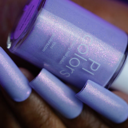 A hand with long, square-shaped nails painted in PI Colors’ Snowball.485, a handmade light purple shimmer nail polish with a subtle pink iridescent sheen, holds the matching bottle labeled "PI Colors.