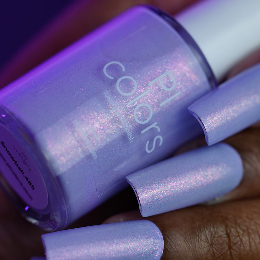 A close-up of a hand with long nails painted in shimmery light purple PI Colors Snowball.485 nail polish, holding a matching bottle under purple lighting.