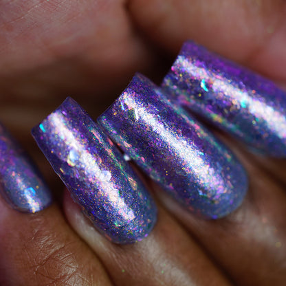 A close-up of fingernails painted with PI Colors’ "Stained Glass.436," a handmade shimmery purple-grey nail polish featuring sparkling multicolored flakie accents and a glossy finish.