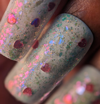 Close-up of fingernails painted with PI Colors' Stormy Hearts.206, featuring a gray base adorned with pink heart-shaped glitter and topped with silver holo glitter. The result is a textured, sparkly finish with multicolored flecks.