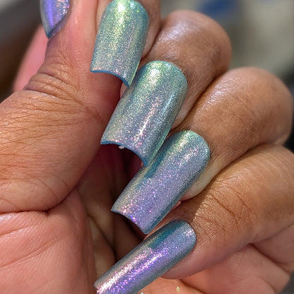 A close-up of a hand with long, square nails painted in PI Colors’ Sugar Sparkles.451, a luxury nail lacquer featuring shimmery, iridescent blue and purple hues with a metallic, holographic shine and an elegant finish.