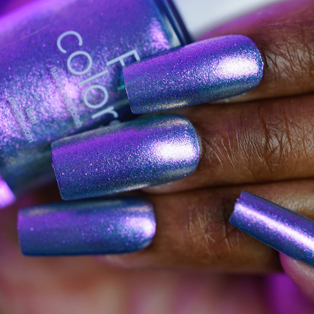 A close-up of a hand with long nails painted in shimmering purple and blue "Sugar Sparkles.451" by PI Colors, holding the matching bottle of luxury nail polish.