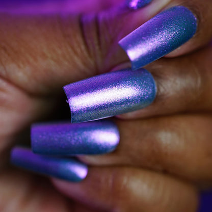 A close-up of a hand with long, coffin-shaped nails painted in PI Colors Sugar Sparkles.451, a luxury nail lacquer featuring a shimmery blue-purple metallic finish under purple lighting.