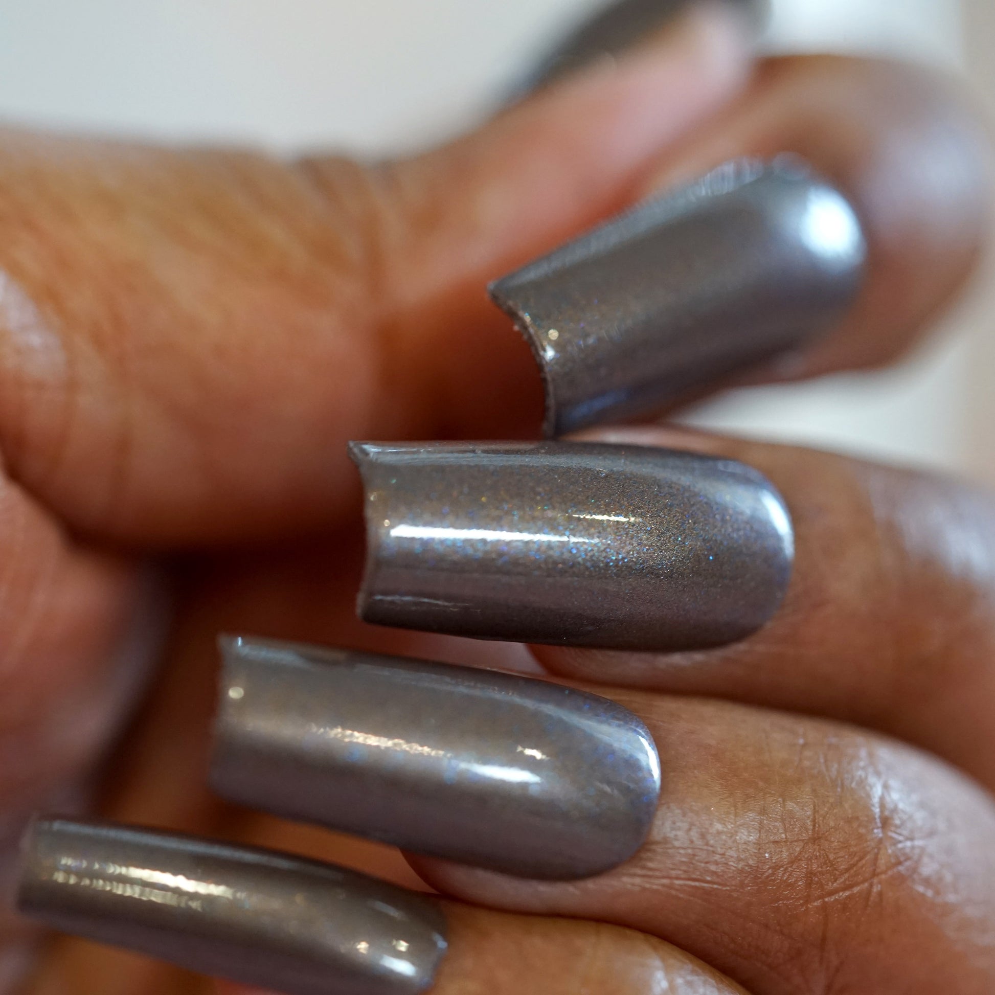 Close-up of a hand showcasing long fingernails painted with a glossy, metallic gray nail polish from PI Colors' luxury collection featuring their Woodland Night.006 brown shade.