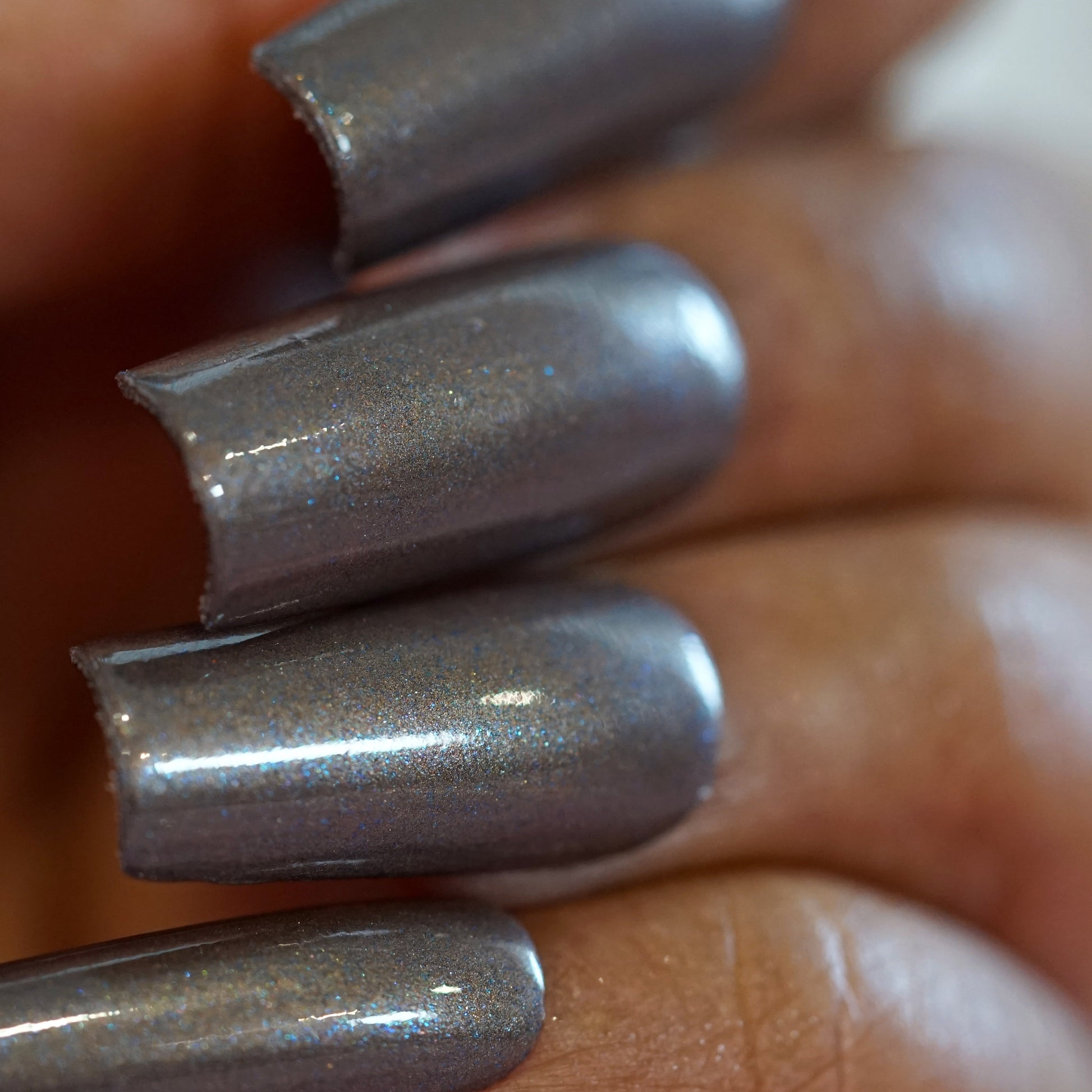 A close-up of a hand showcases nails polished in the sophisticated Woodland Night.006 shade from PI Colors. The long, expertly manicured nails glisten subtly as they catch the light, highlighting their metallic brown hue with a hint of shimmer from this luxury nail lacquer.